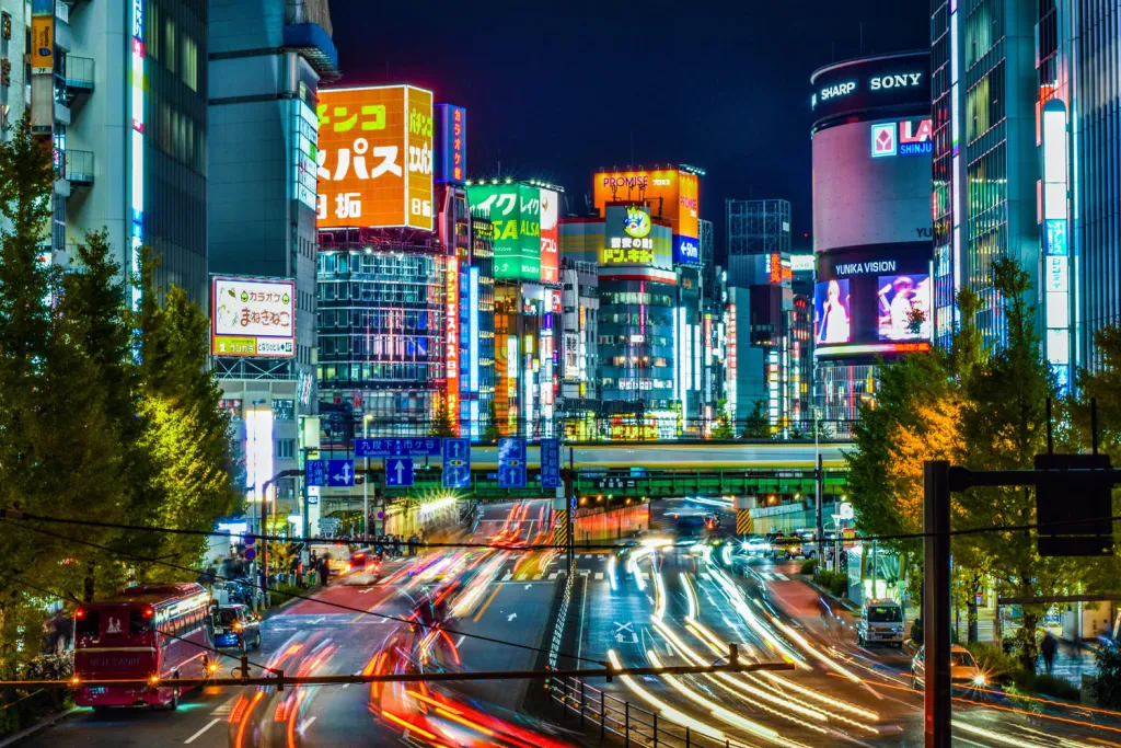 Sakura-liveried bullet train carrying shopping carts through neon Tokyo at dusk