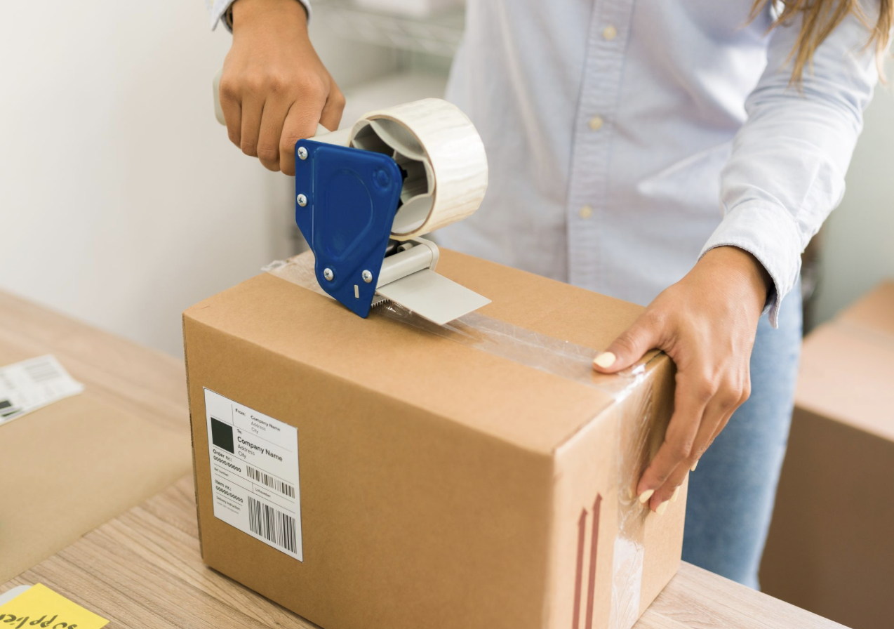 Hands taping and labelling a packed cardboard parcel ready to ship